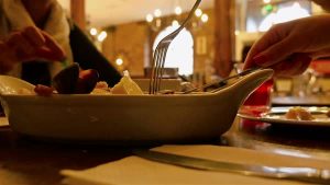 A restaurant table,a plate with food and people holding utensils
