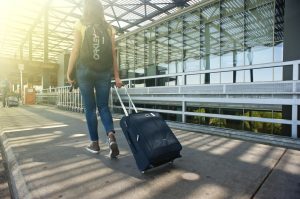 A girl who understands why people move to Brazil and wants to be one of them, walking through an airport with a backpack and a suitcase